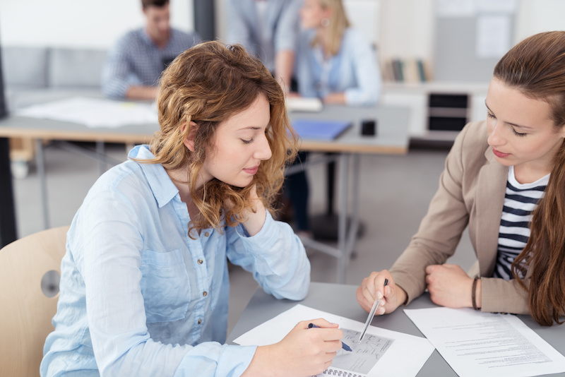 junge frau erklärt einer studentin etwas in den unterlagen