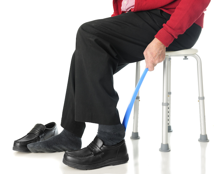 Close-up view of a senior man sliding into his loafers with the aid of a long-handled shoe horn.  On a white background.